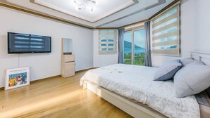 Un dormitorio con una cama, un televisor de pantalla plana, una obra de arte enmarco y una ventana con persianas.