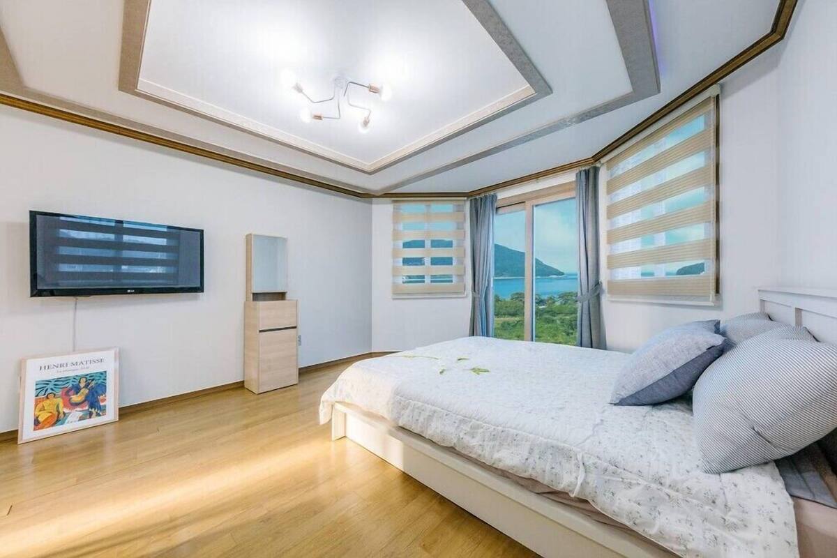 Un dormitorio con una cama, un televisor de pantalla plana, una obra de arte enmarco y una ventana con persianas.