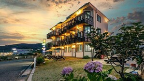 Un hotel de varios pisos con balcones, mobiliario exterior y un jardín ajardinado.