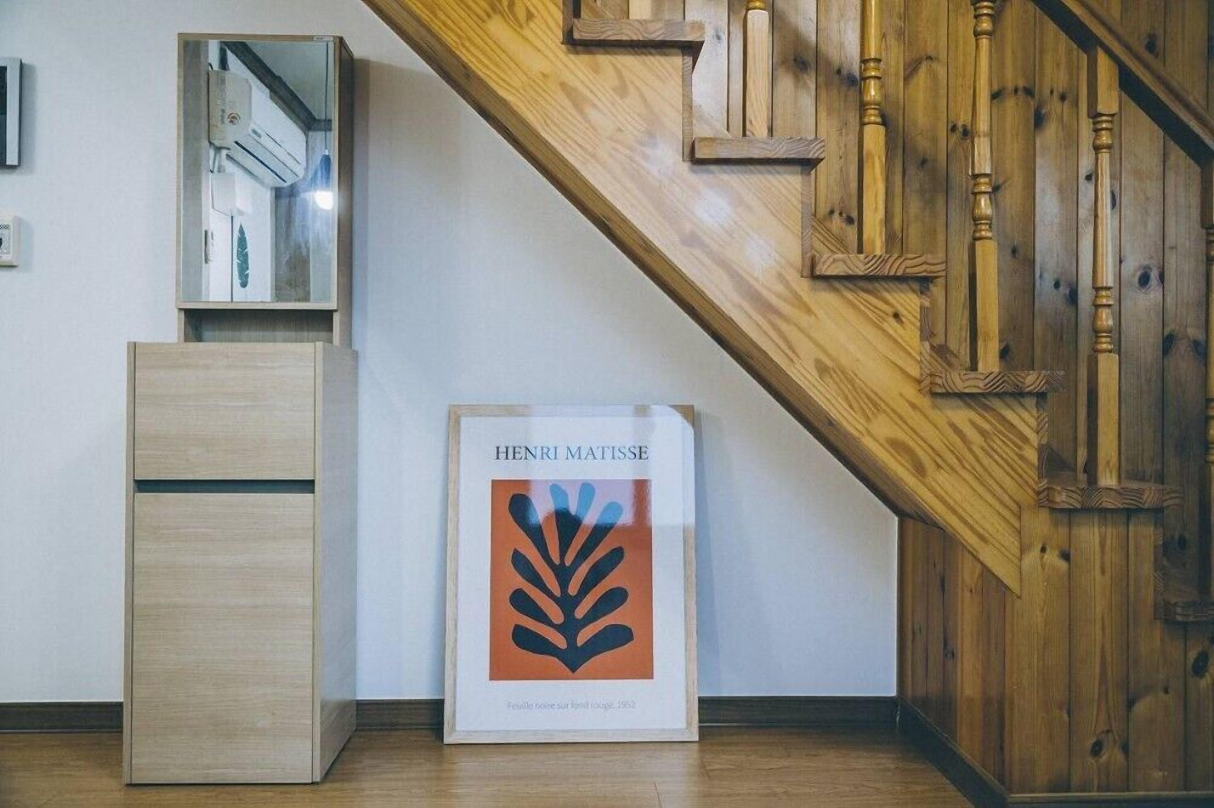 A framed Henri Matisse artwork, a wooden cabinet, and a staircase with wooden railings.