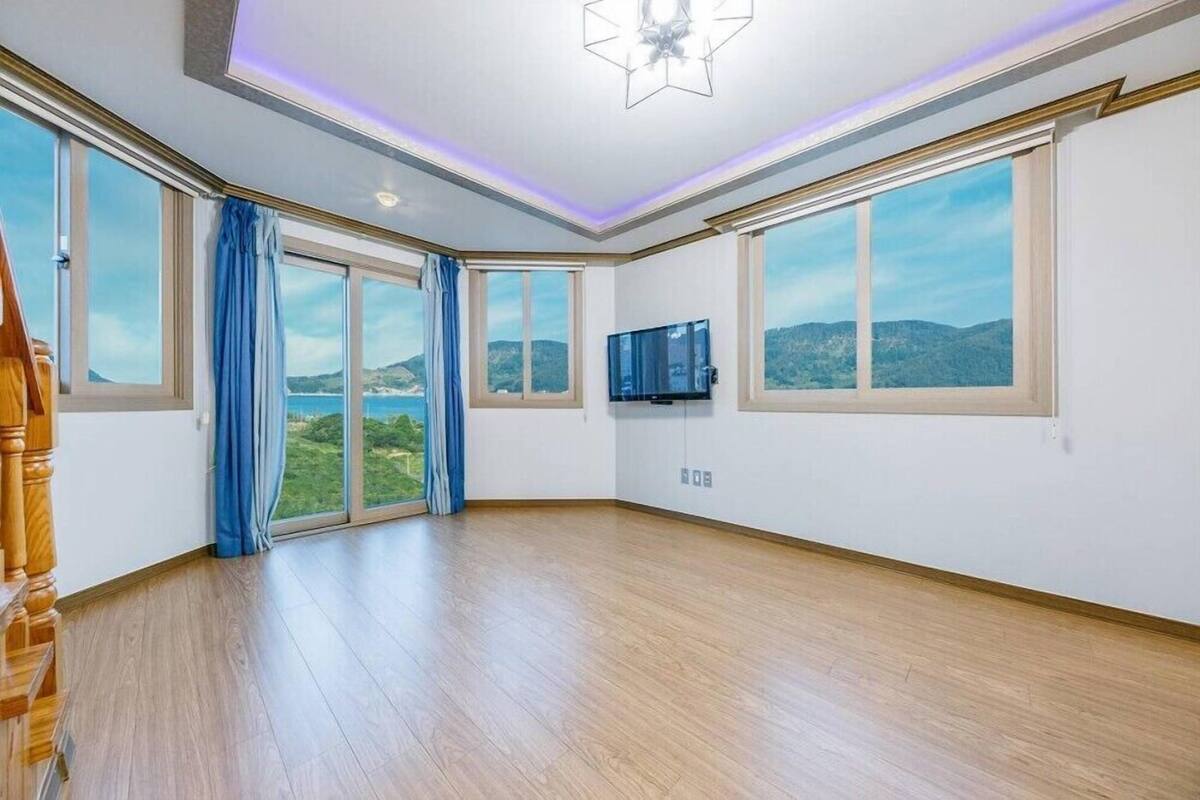 Una habitación amplia con ventanas grandes, un televisor de pantalla plana y una escalera de madera.