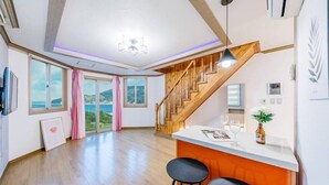 Un espacio habitable amplio con una escalera de madera, una isla en la cocina y ventanas grandes que ofrecen vistas al exterior.
