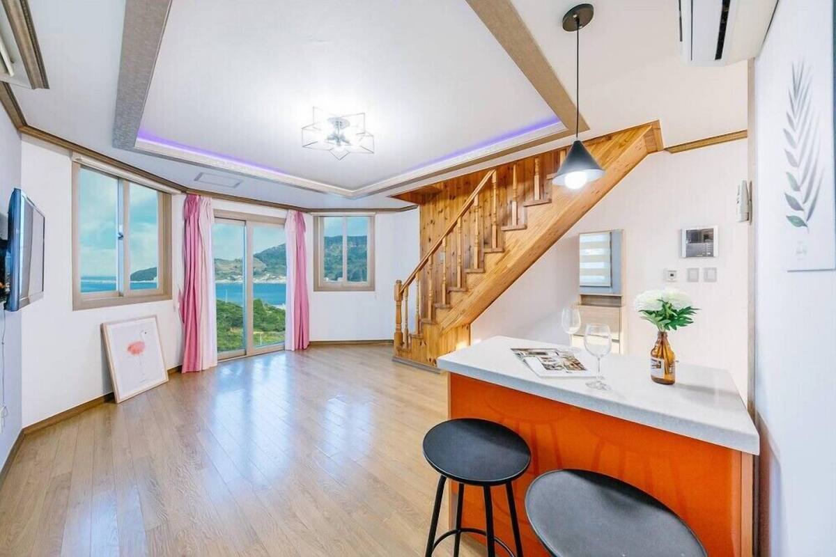 Un espacio habitable amplio con una escalera de madera, una isla en la cocina y ventanas grandes que ofrecen vistas al exterior.