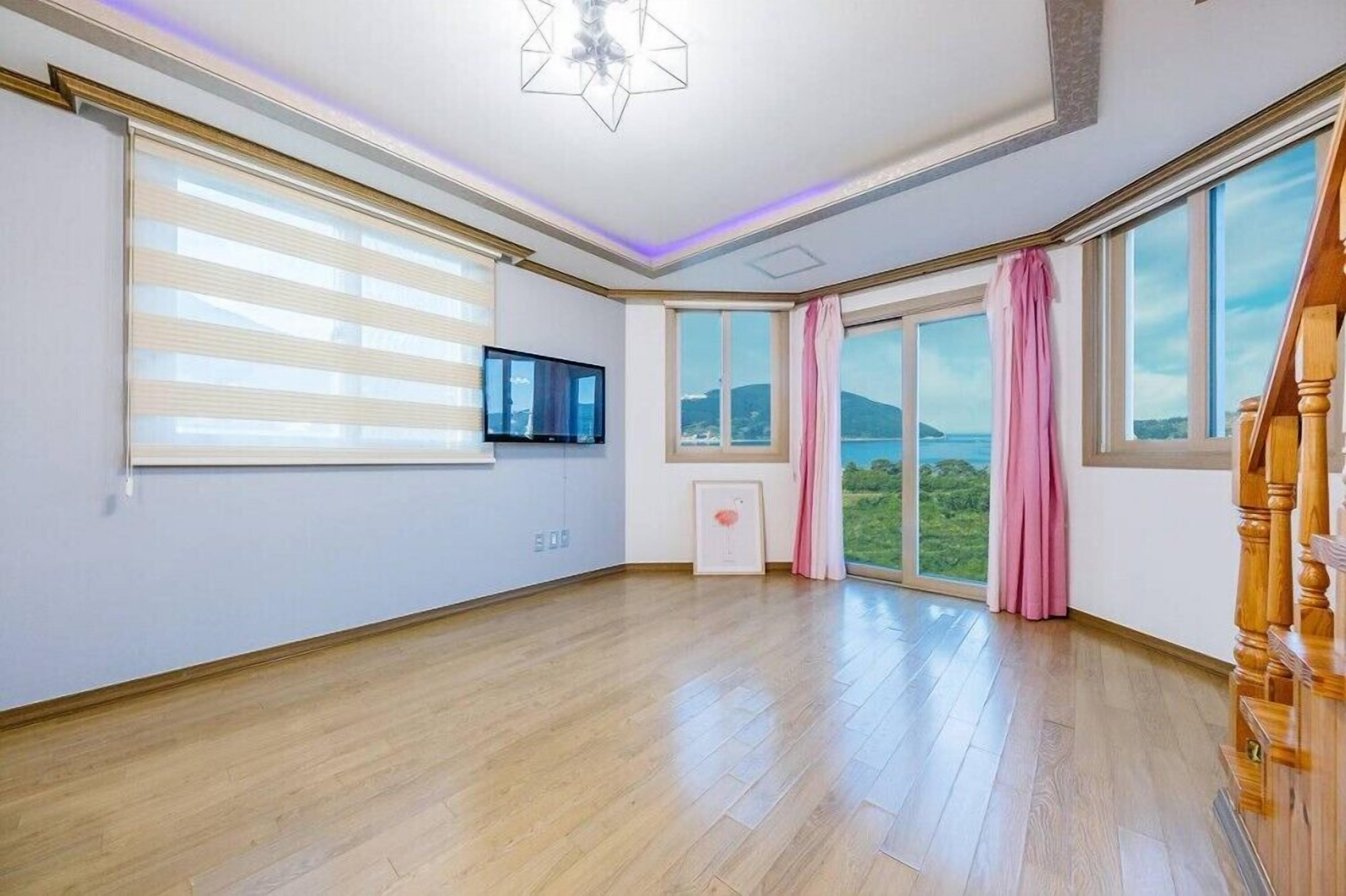 A spacious room with large windows, a flat-screen TV, and a wooden staircase.