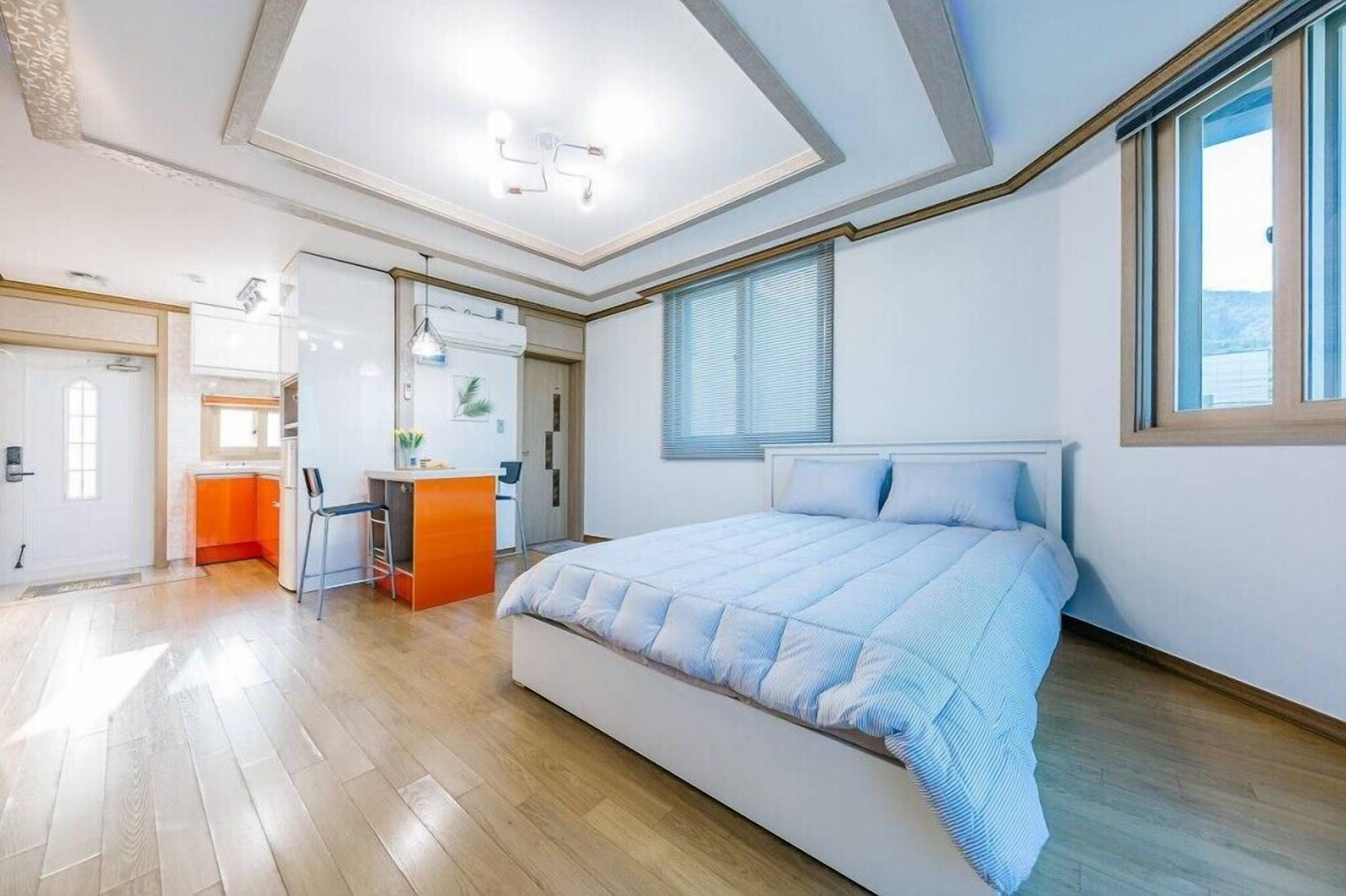 A modern bedroom with a large bed, a desk, and a bathroom.