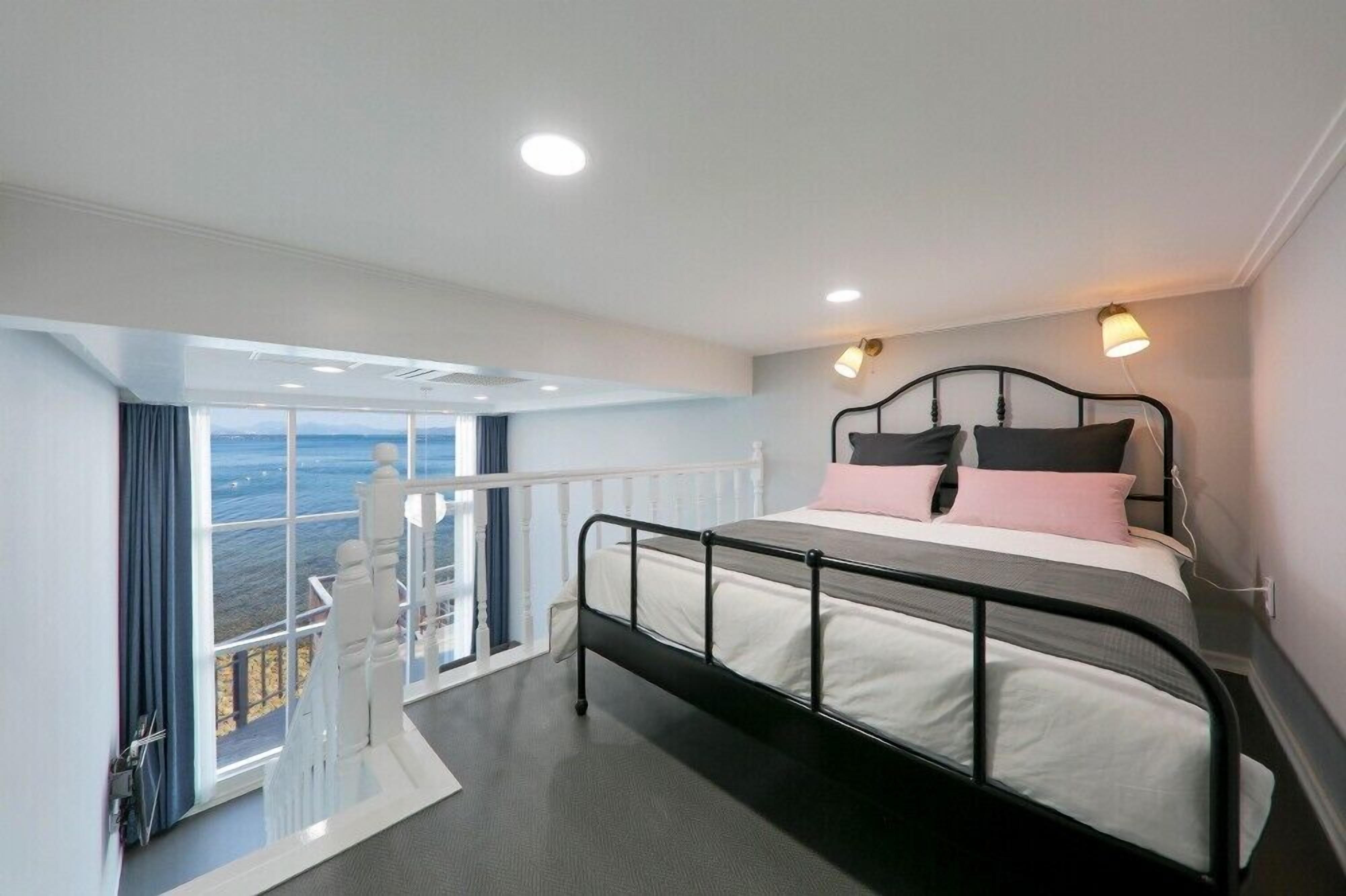 A modern bedroom with a balcony, a bed with white and pink bedding, and a view of the sea.