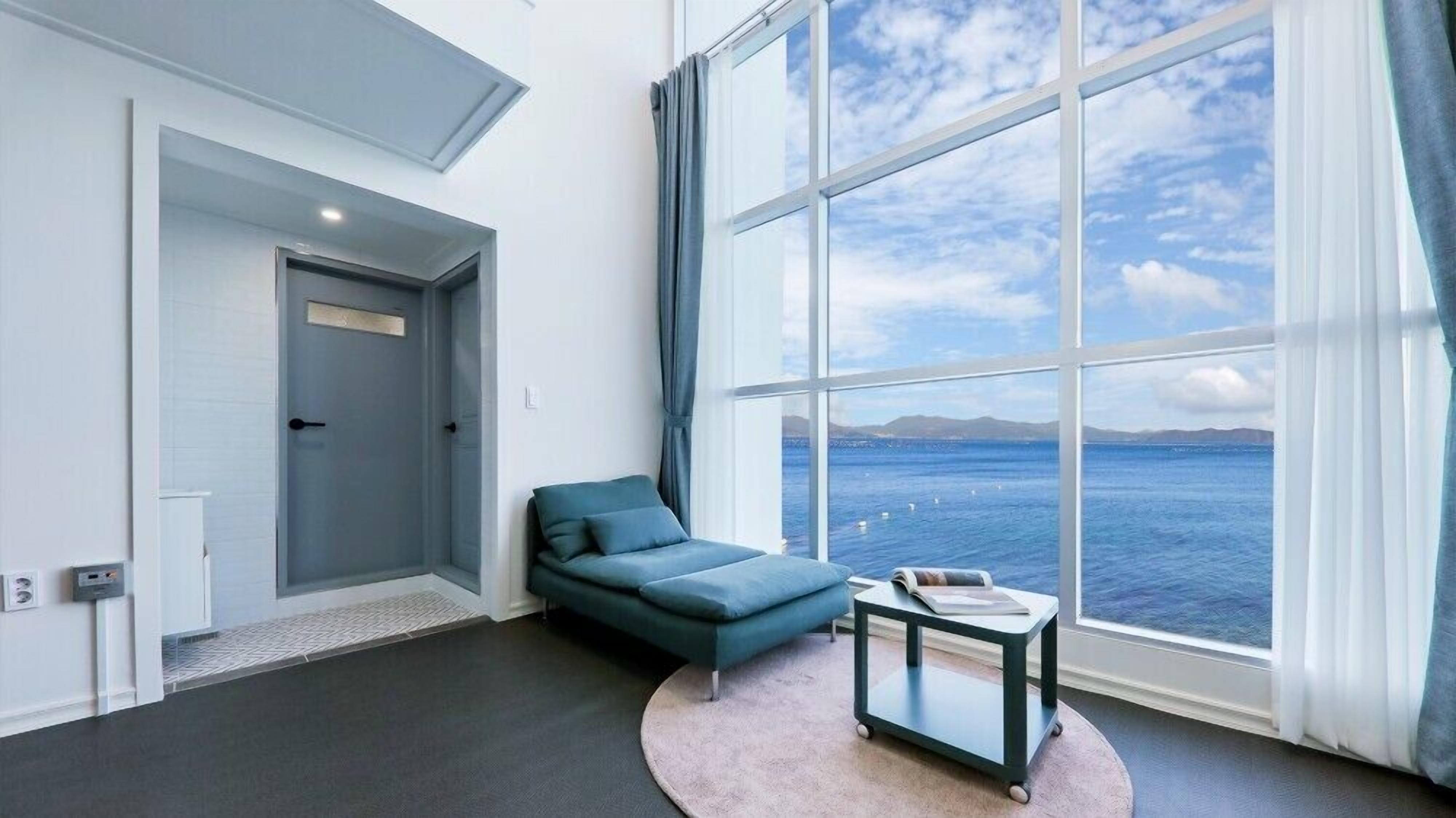 A modern room with a large window offering a view of the sea, a sofa, a small table, and a door.