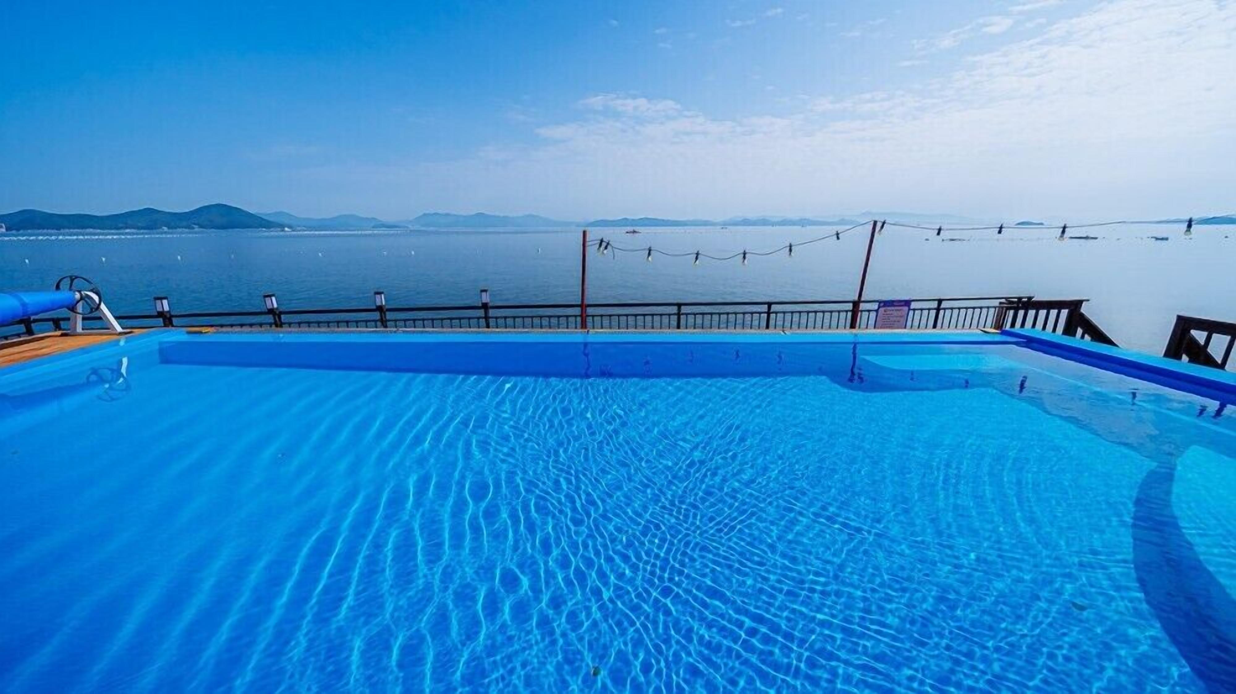 A pool with clear blue water, a wooden deck, and a view of the sea and distant mountains.