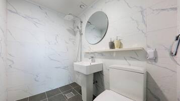 Un baño con inodoro blanco, lavamanos y ducha.