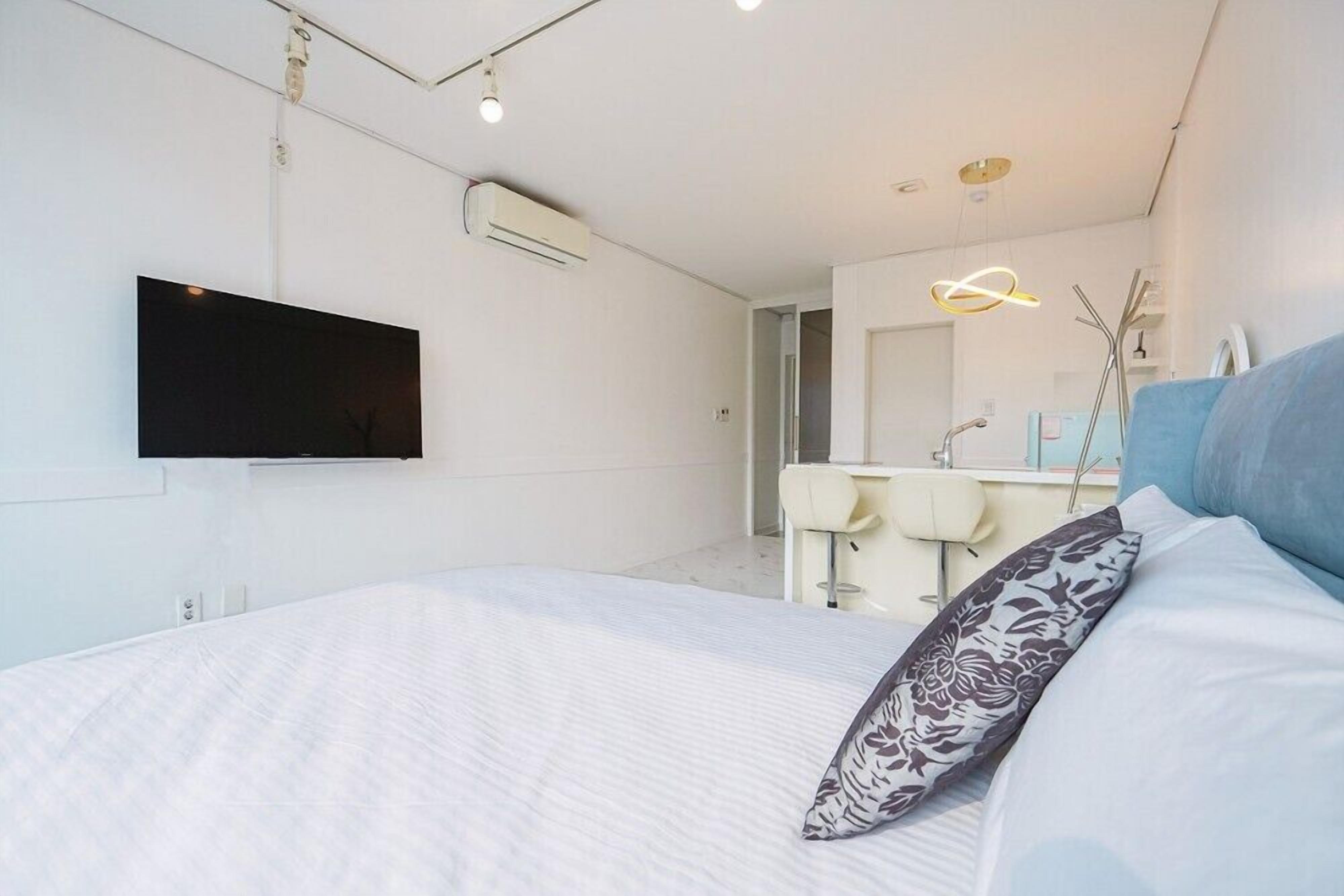 Een moderne slaapkamer met een bed, een flatscreen televisie, een badkamer met een spiegel en een wastafel.