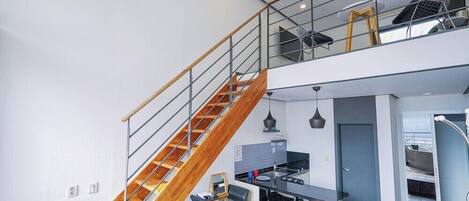 A modern kitchen with a central island, a staircase with wooden steps, and a mezzanine level with seating.