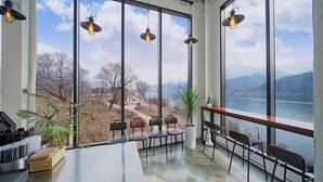 Un comedor con amplios ventanales y vistas a un lago, con varias sillas.