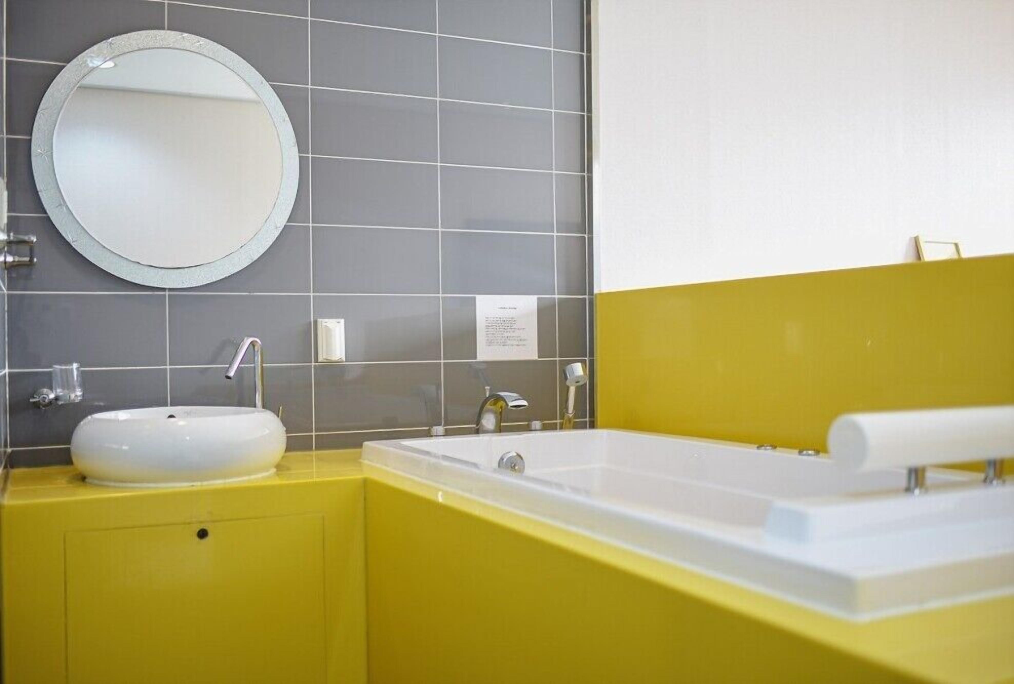 Une salle de bain avec un miroir rond, un lavabo blanc et une baignoire.