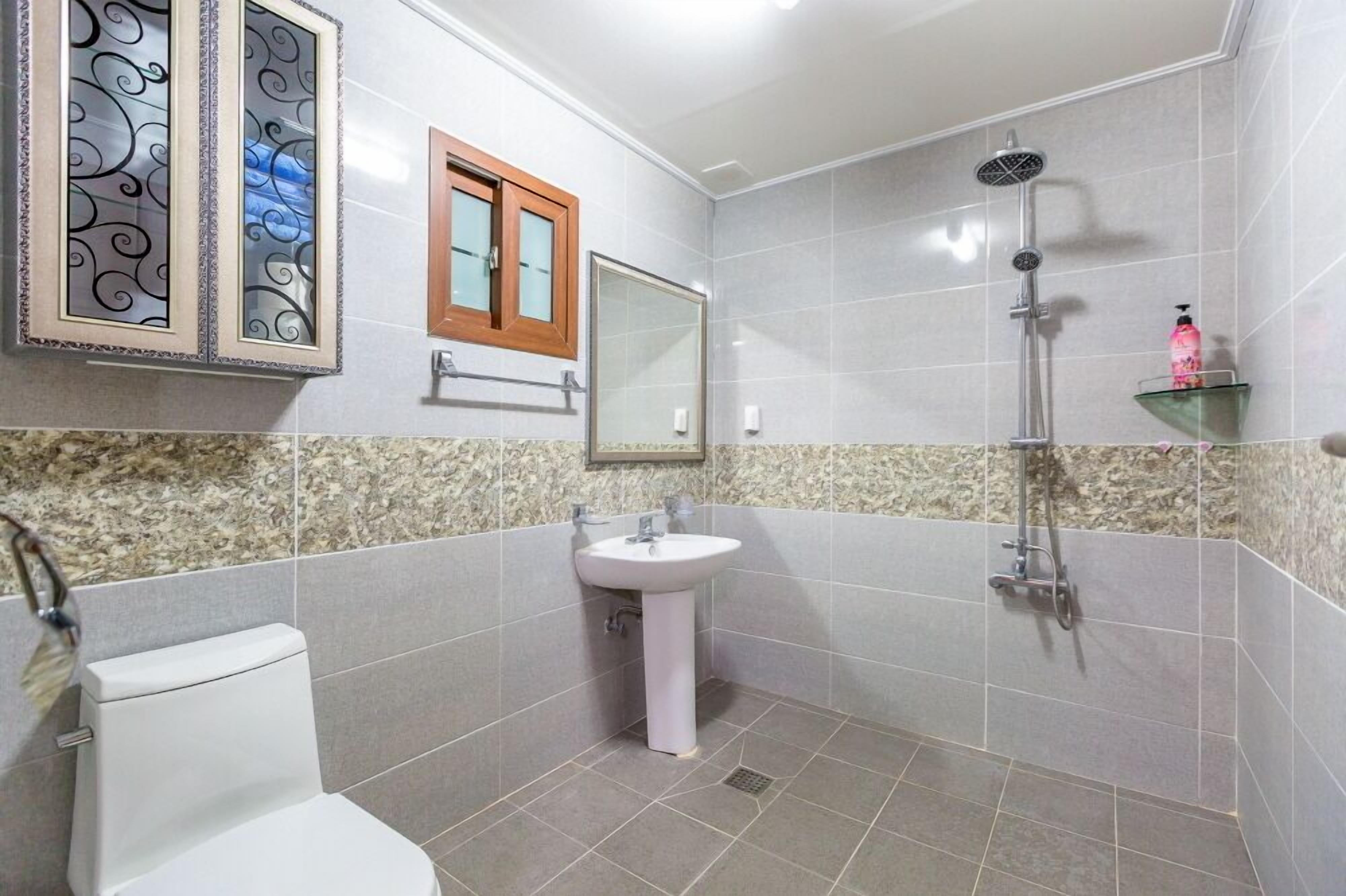 Un bagno con toilette, lavandino, doccia, uno specchio decorativo e un piccolo ripiano con articoli da toilette.