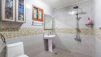 Un bagno con toilette, lavandino, doccia, uno specchio decorativo e un piccolo ripiano con articoli da toilette.