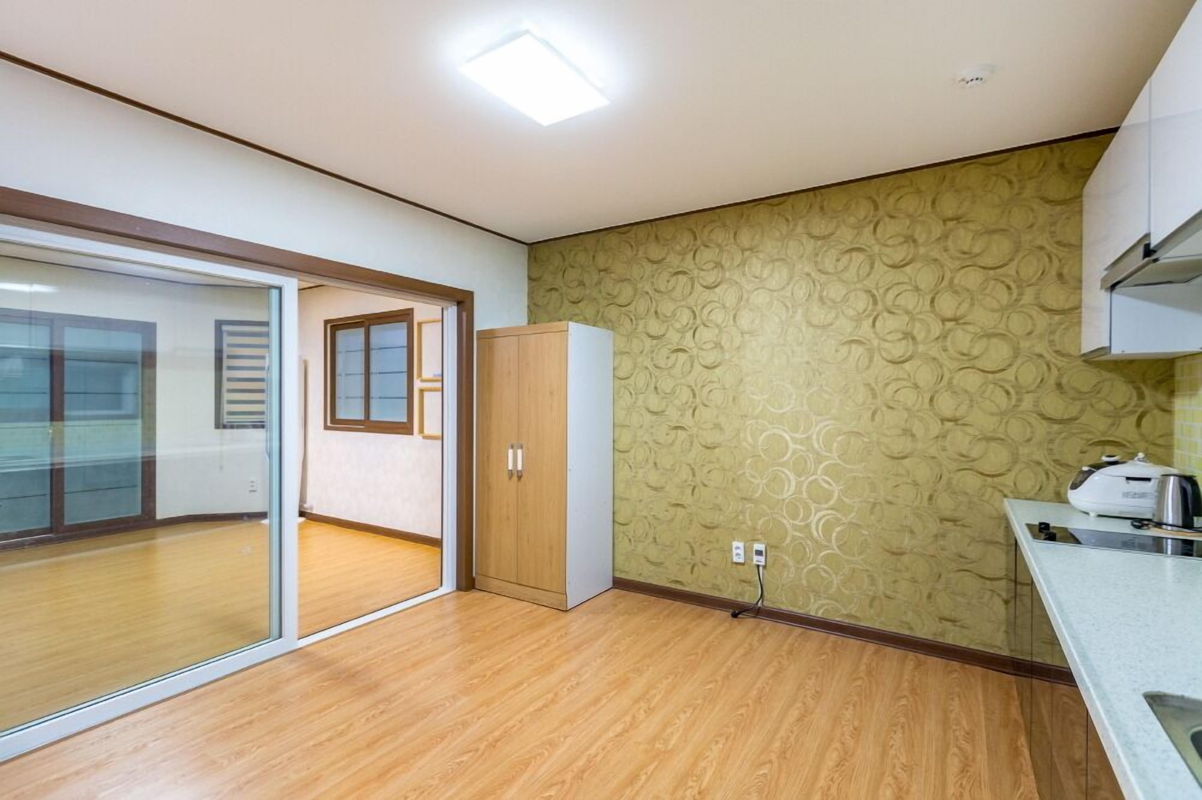Habitación con puerta de cristal corredera que da a un balcón, un armario de madera y una zona de cocina con encimera y fregadero.