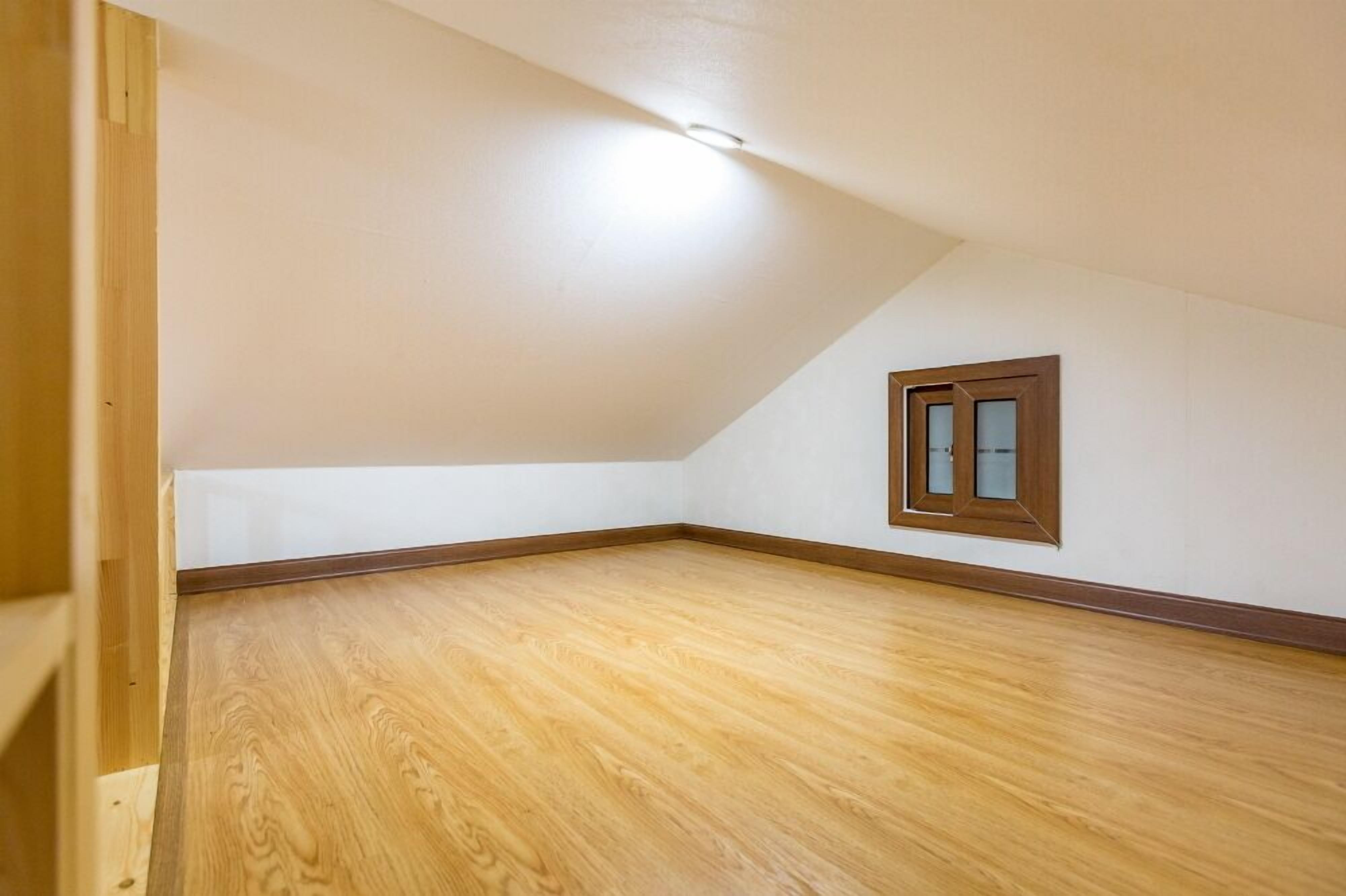 Ein leerer Raum mit Holzboden, weißen Wänden und einer geneigten Decke.