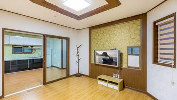 Una habitación con piso de madera, una lámpara en el techo, un televisor montado en una pared con diseño y una puerta corrediza que da a una cocina.