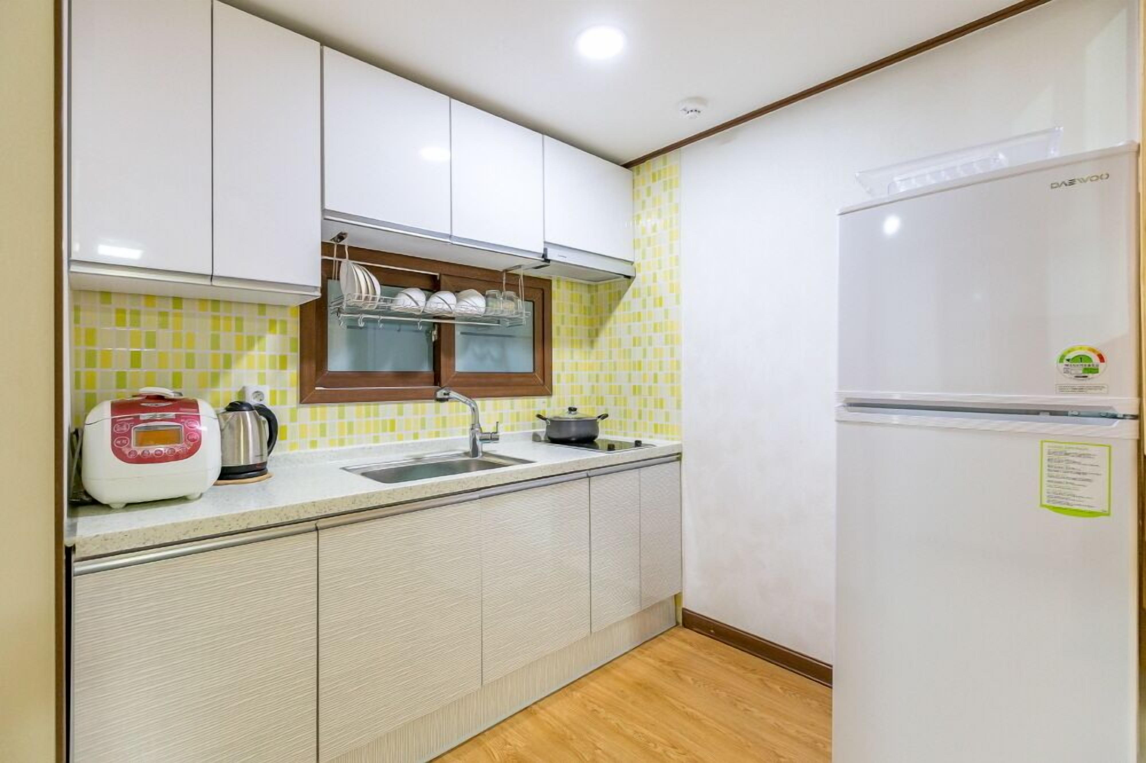A compact kitchen with white cabinets, a sink, a stove, a rice cooker, and a refrigerator.