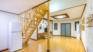 A spacious room with a wooden staircase, a white refrigerator, and a wall with framed pictures. - Neulpureun Pension (Yeongdeok)