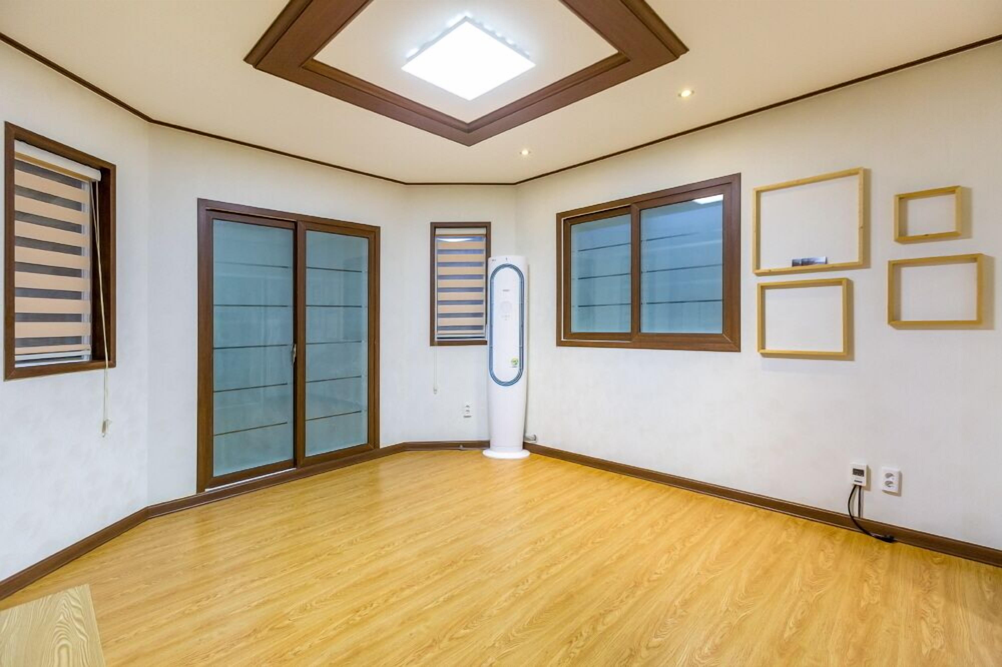 A spacious room with wooden flooring, large sliding glass doors, a central air conditioning unit, and framed pictures on the wall.
