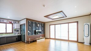 A spacious room with a wooden floor, a built-in kitchen area, a large sliding glass door, and a ceiling fan. - Neulpureun Pension (Yeongdeok)