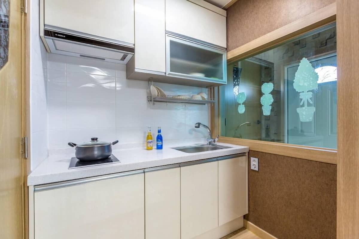 Una cocina compacta con armarios blancos, estufa integrada, un lavamanos y un ventanal con detalles decorativos.