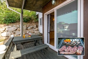 An outdoor patio with a wooden table, a stone wall, and a grill with various meats. - Woori pension (Yeongdeok)