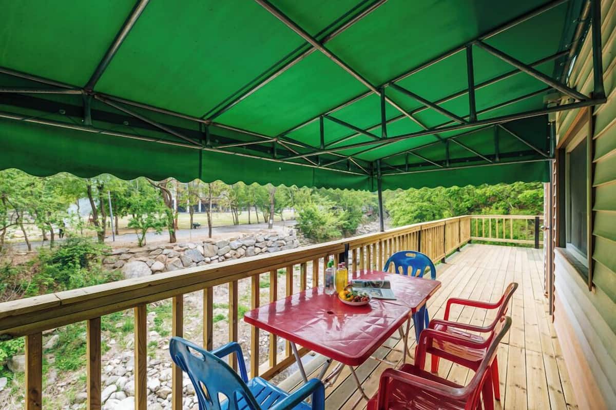 A covered outdoor deck with a table and chairs, a green canopy, and a view of a landscaped garden.