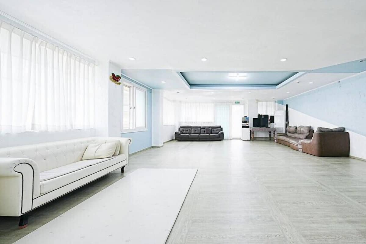 A spacious, modern living area with a white sofa, a dark leather sofa, and a dining area with a TV and kitchen appliances.