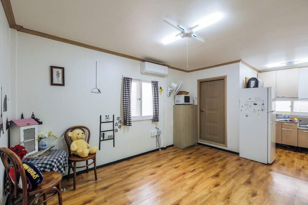 A compact living space with a kitchen area, a dining table with chairs, a ceiling fan, and a refrigerator.