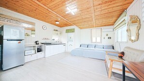 A cozy, well-lit room with a wooden ceiling, a kitchenette, a bed with a blue and white bedspread, and a small table with a teddy bear. - Mulga Pension (Gapyeong)