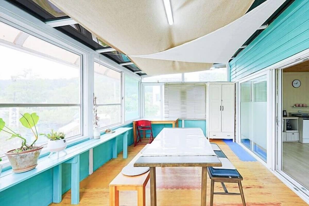 A bright, open-plan kitchen and dining area with large windows, a wooden table, and a bench.