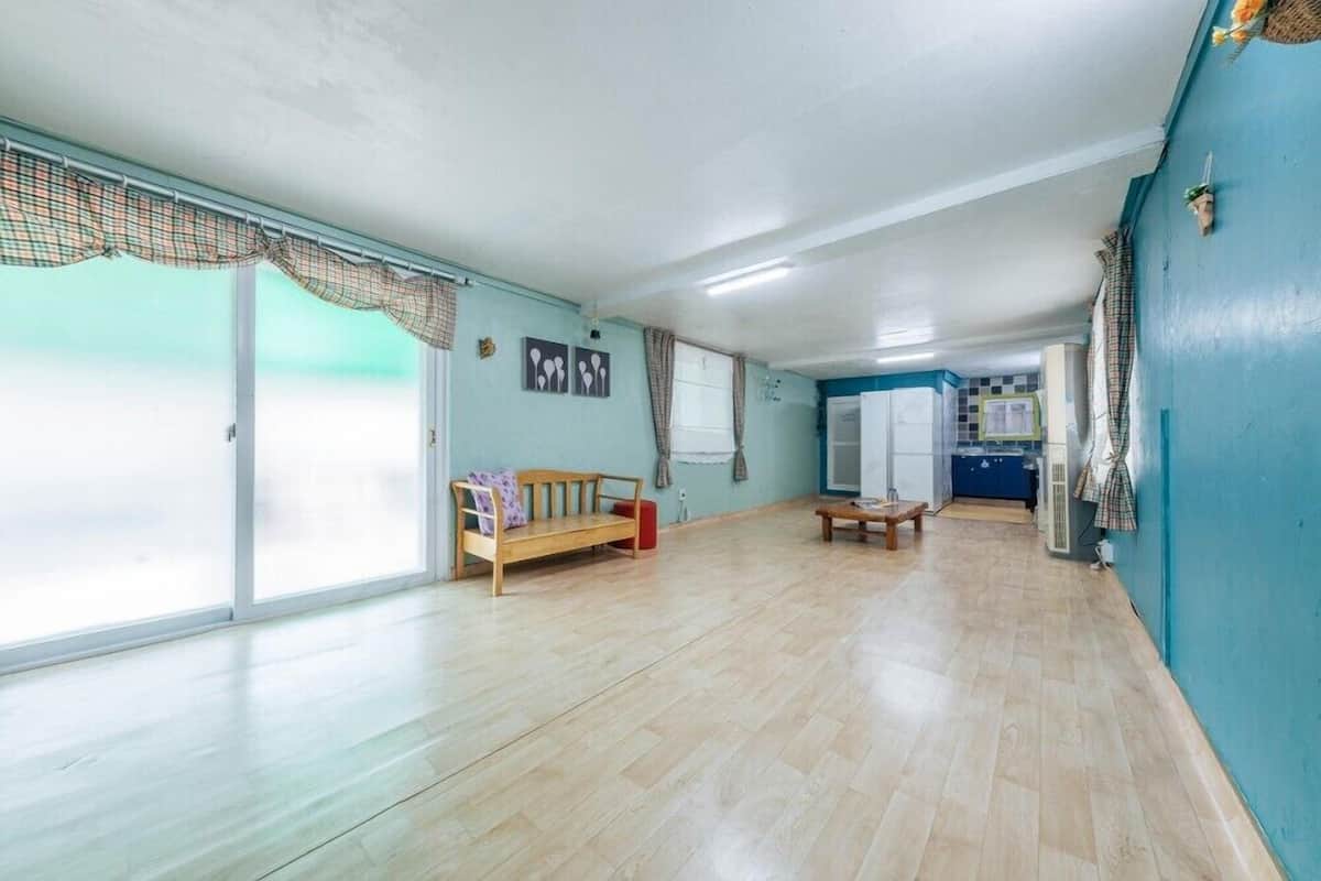 A spacious room with a large sliding glass door, a wooden bench, a small table, and a kitchenette in the background.