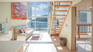 A spacious living area with a large window, a wooden staircase, and a view of the sea. - Dream Pension (Tongyeong)