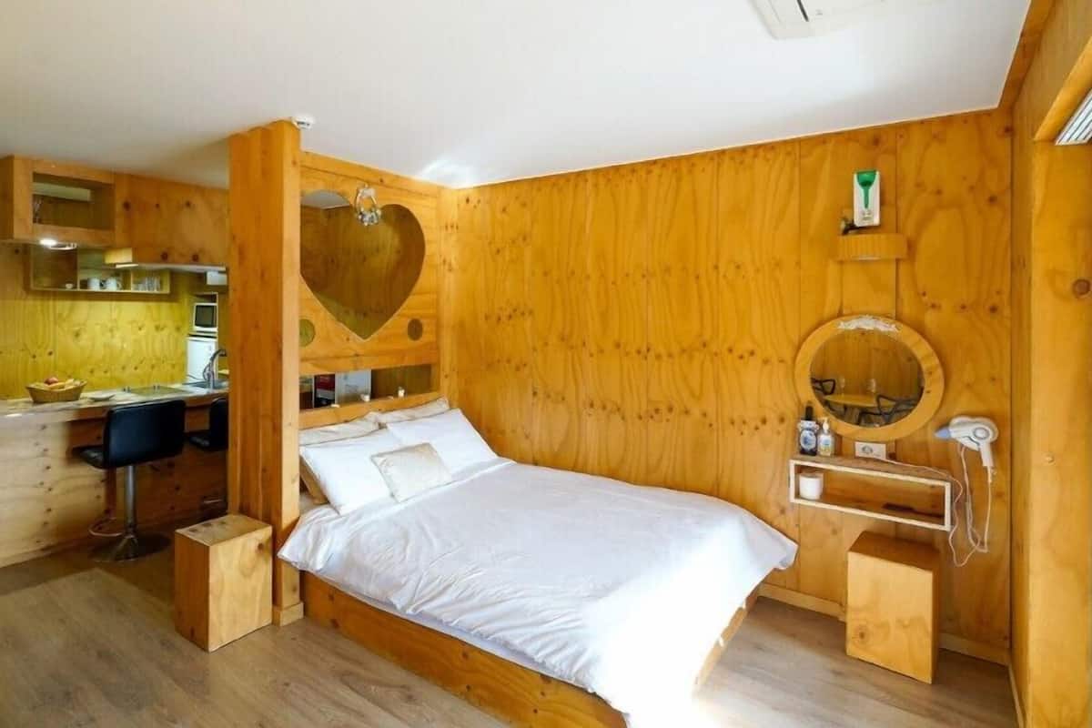 A wooden-themed bedroom with a bed, a desk, and a vanity area.