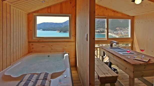 A wooden cabin with a hot tub, a dining area with a view of the sea, and a wooden deck. - Pado Hyanggi Pension (Geoje)