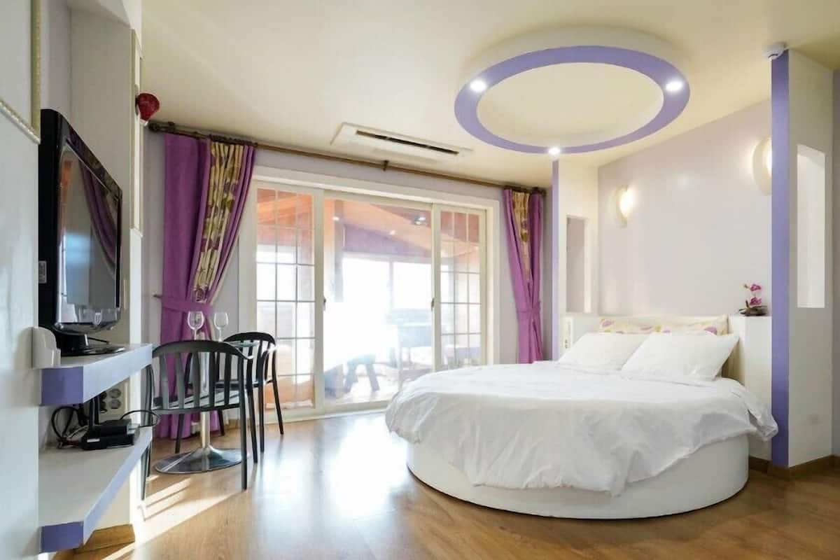 A modern bedroom with a round bed, a television, and a desk with a chair.