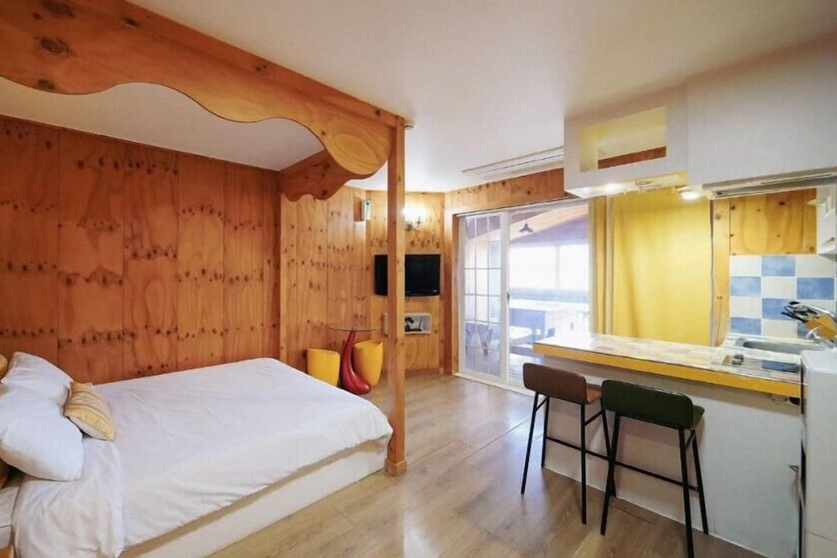 A wooden cabin with a bed, a small kitchen area, and a sliding glass door leading to an outdoor deck.
