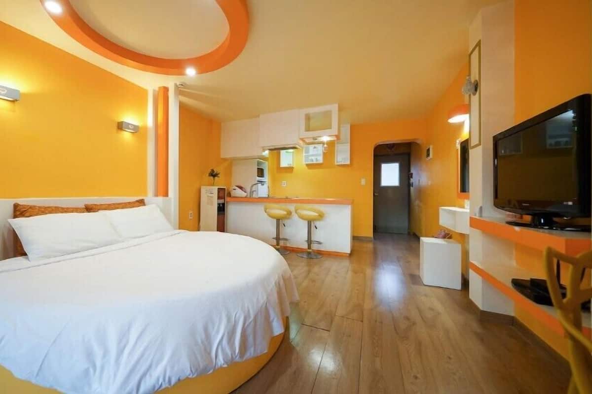 A hotel room with a large bed, a kitchenette, a TV, and a small bar area.
