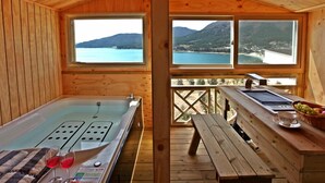 A wooden cabin with a hot tub, wooden deck, and a view of a lake and mountains. - Pado Hyanggi Pension (Geoje)