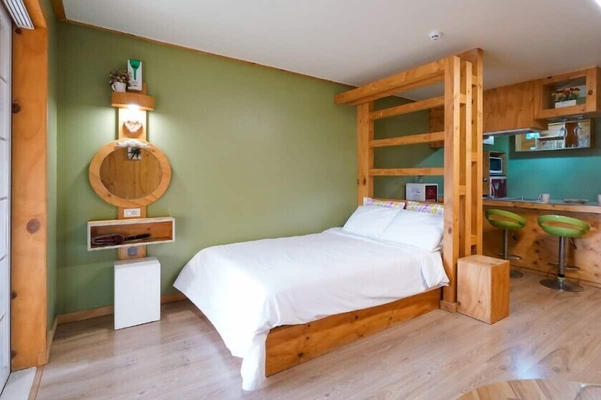 A wooden-framed bedroom with a bed, a small desk, and two green stools.