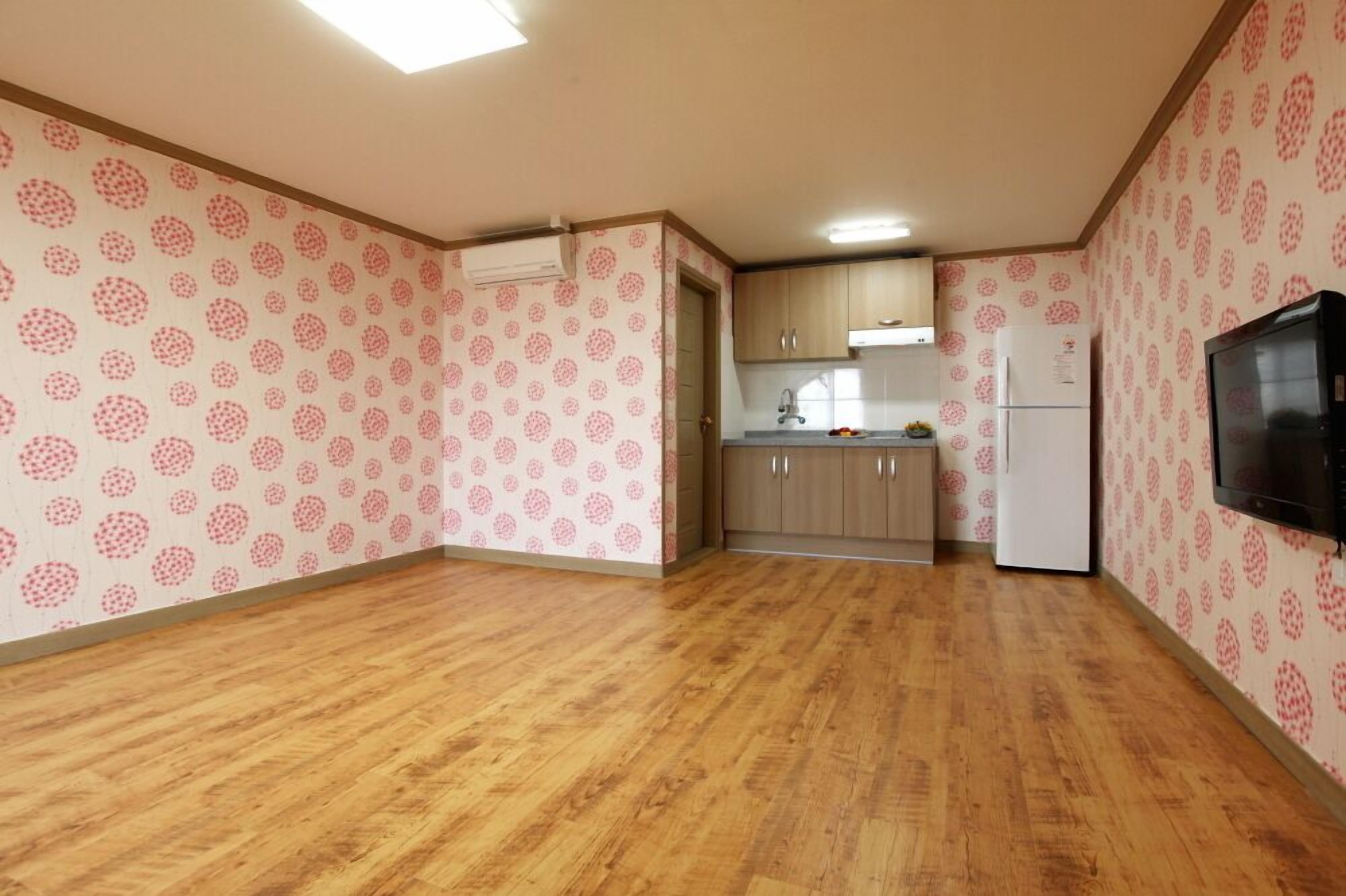 A kitchen with patterned wallpaper, wooden flooring, and basic cabinetry.