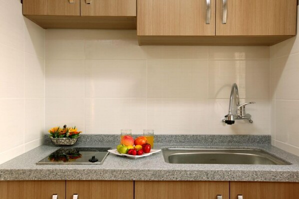 Una cocina con encimeras de granito, pileta de acero inoxidable, gabinetes de madera y un frutero con manzanas y naranjas.