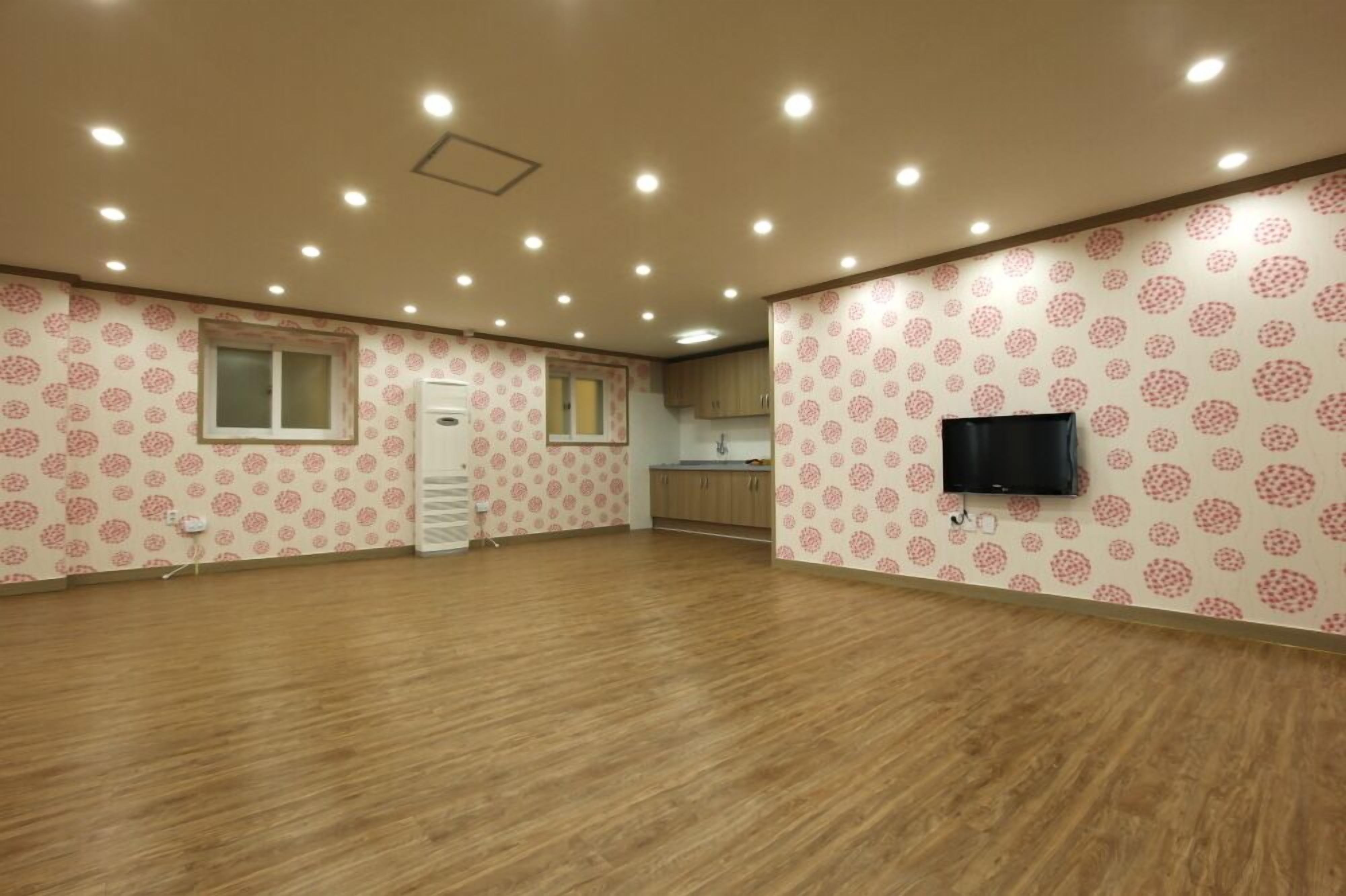 A spacious room with patterned wallpaper, a flat-screen TV mounted on the wall, and a wooden floor.