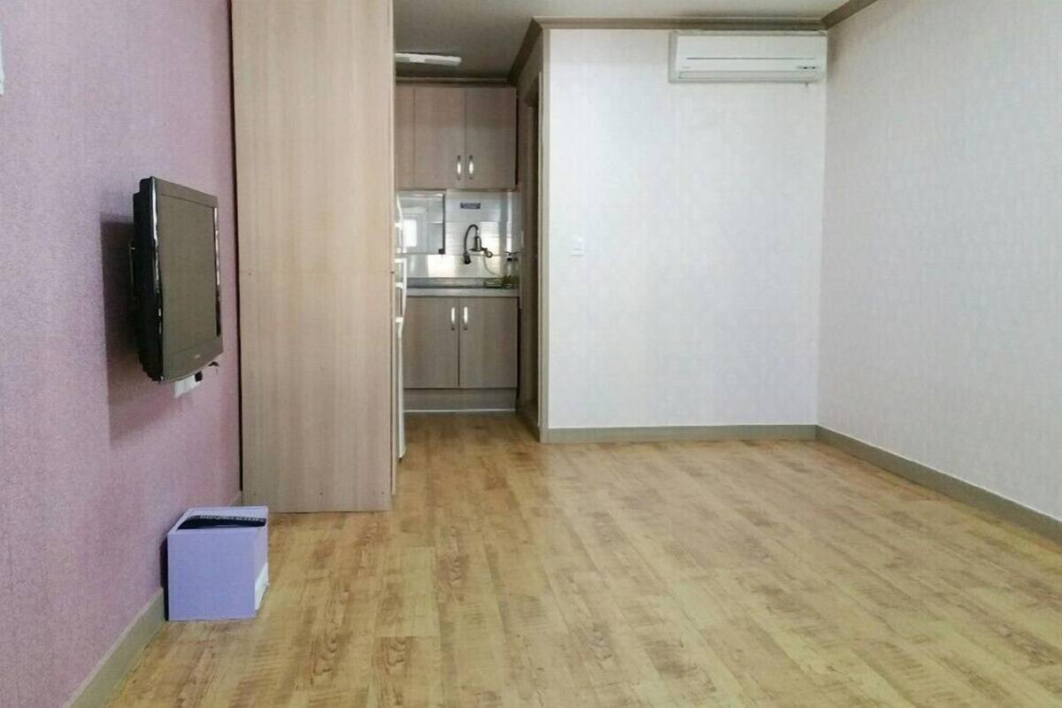 A room with a wooden floor, a television mounted on the wall, and a small trash bin.