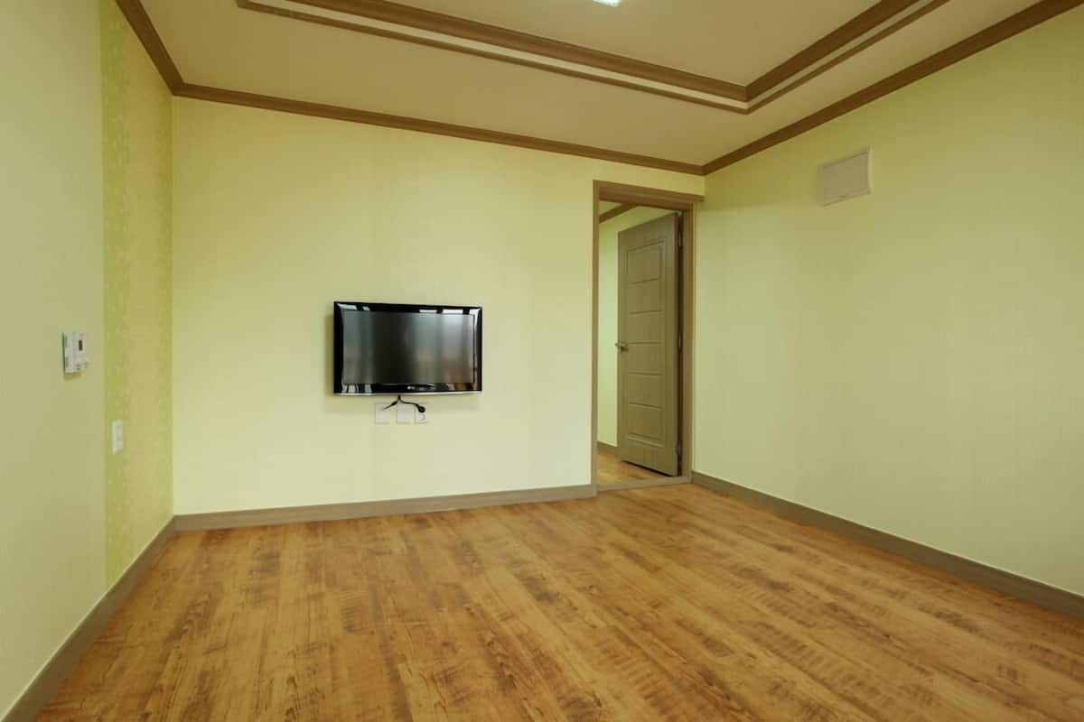 A room with a wooden floor, a mounted flat-screen TV, and a door leading to another room.