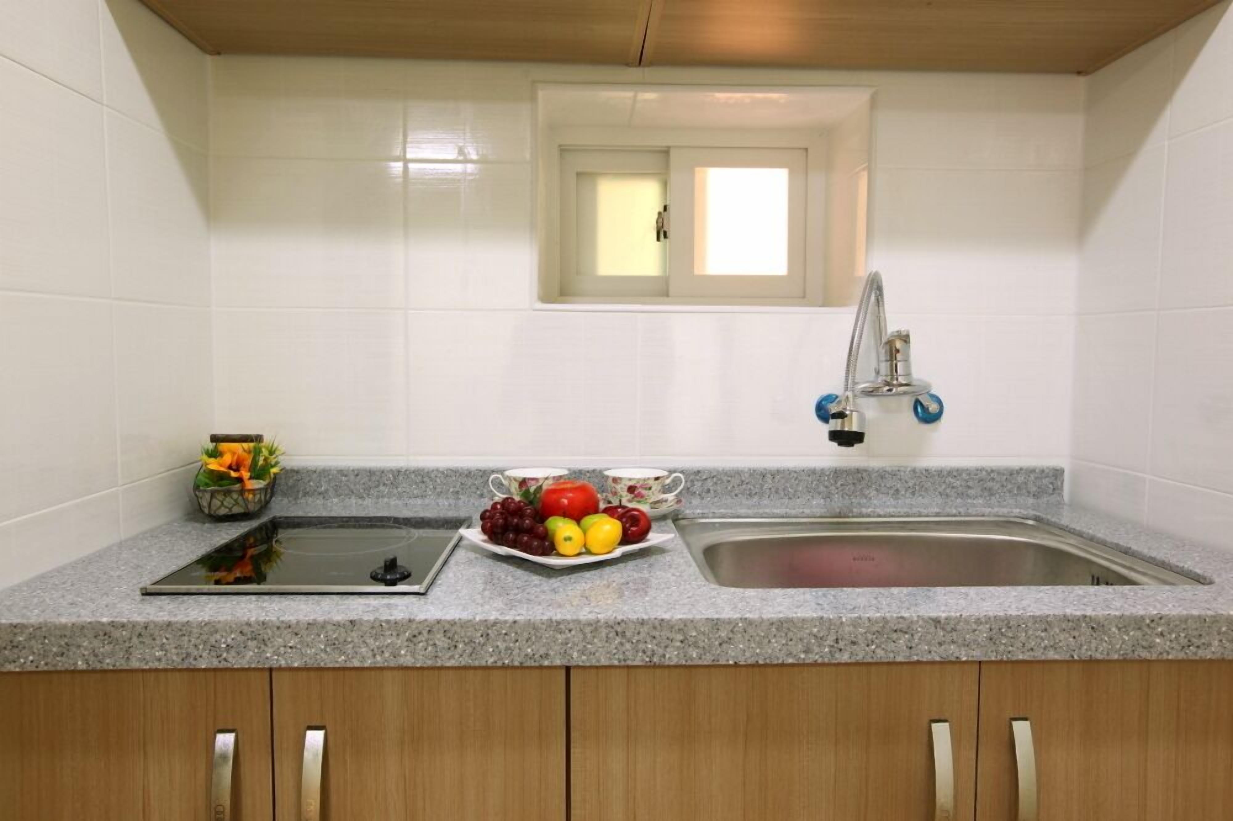 A kitchen with white tiles, a granite countertop, a sink, a window, and a fruit bowl.