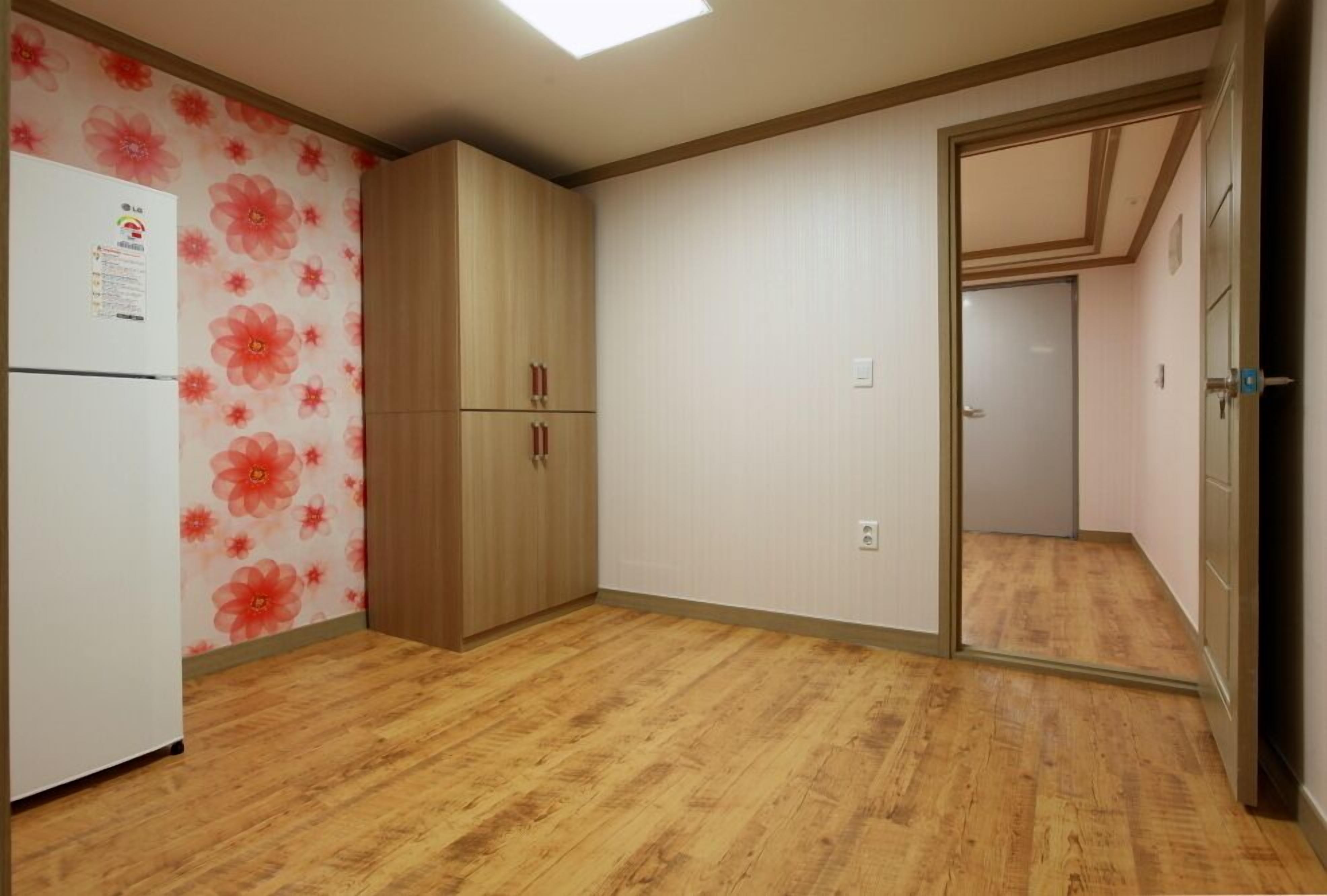 Een kamer met houten vloer, een witte koelkast en een houten garderobe.
