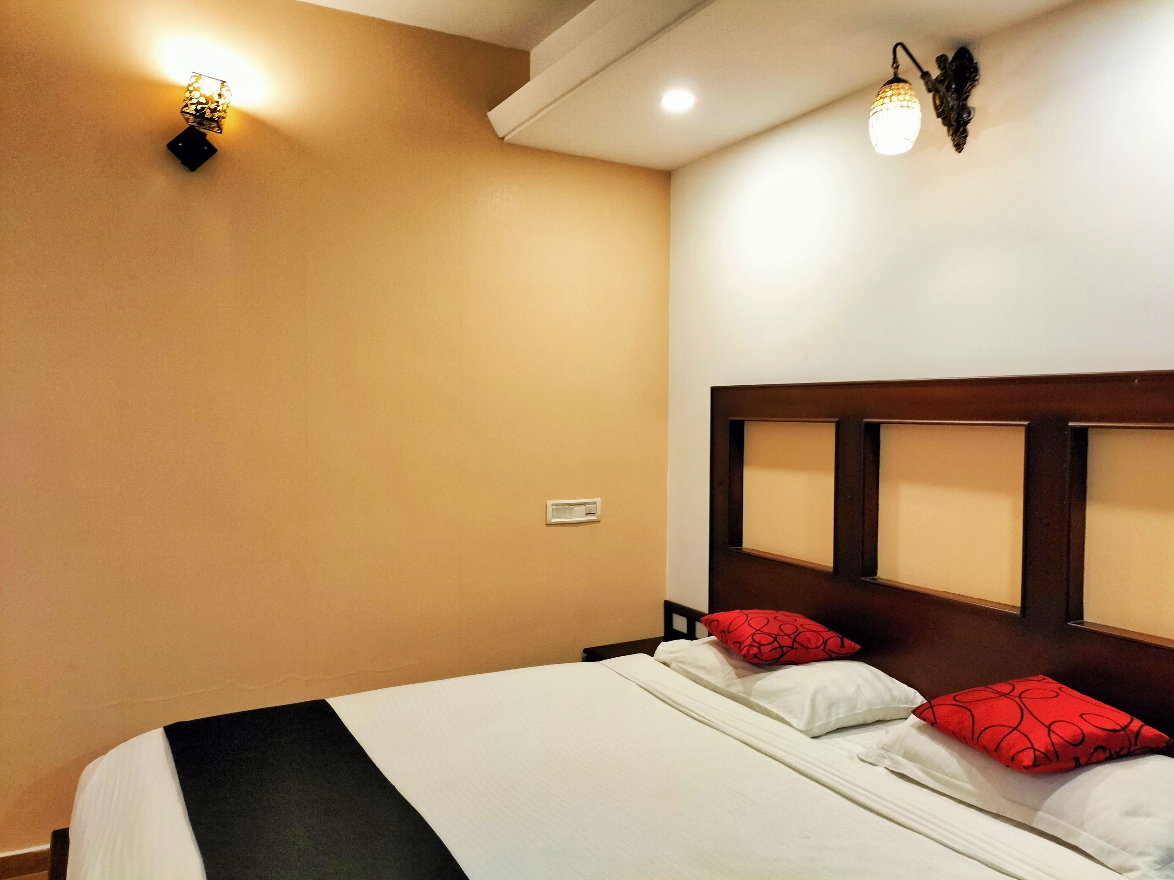 Habitación de hotel con una cama grande, dos almohadas, una mesita de noche y un aplique de pared.